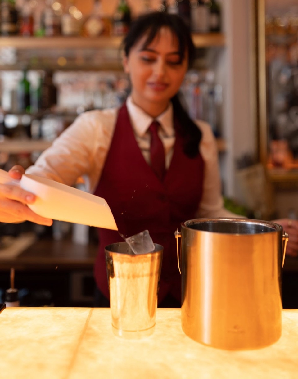 A bartender mixing a drink behind the lit bar